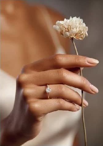 A delicate diamond solitaire ring worn while holding a dried flower