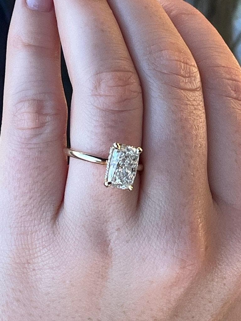 Radiant-cut diamond solitaire with a hidden halo on a thin yellow gold band, worn