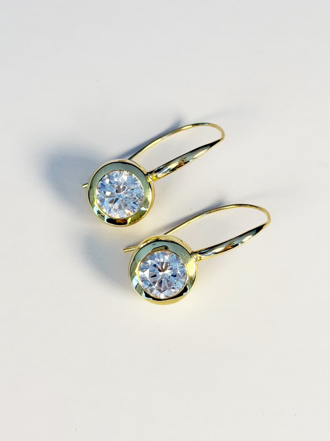 Round brilliant diamonds bezel-set in yellow gold drop earrings