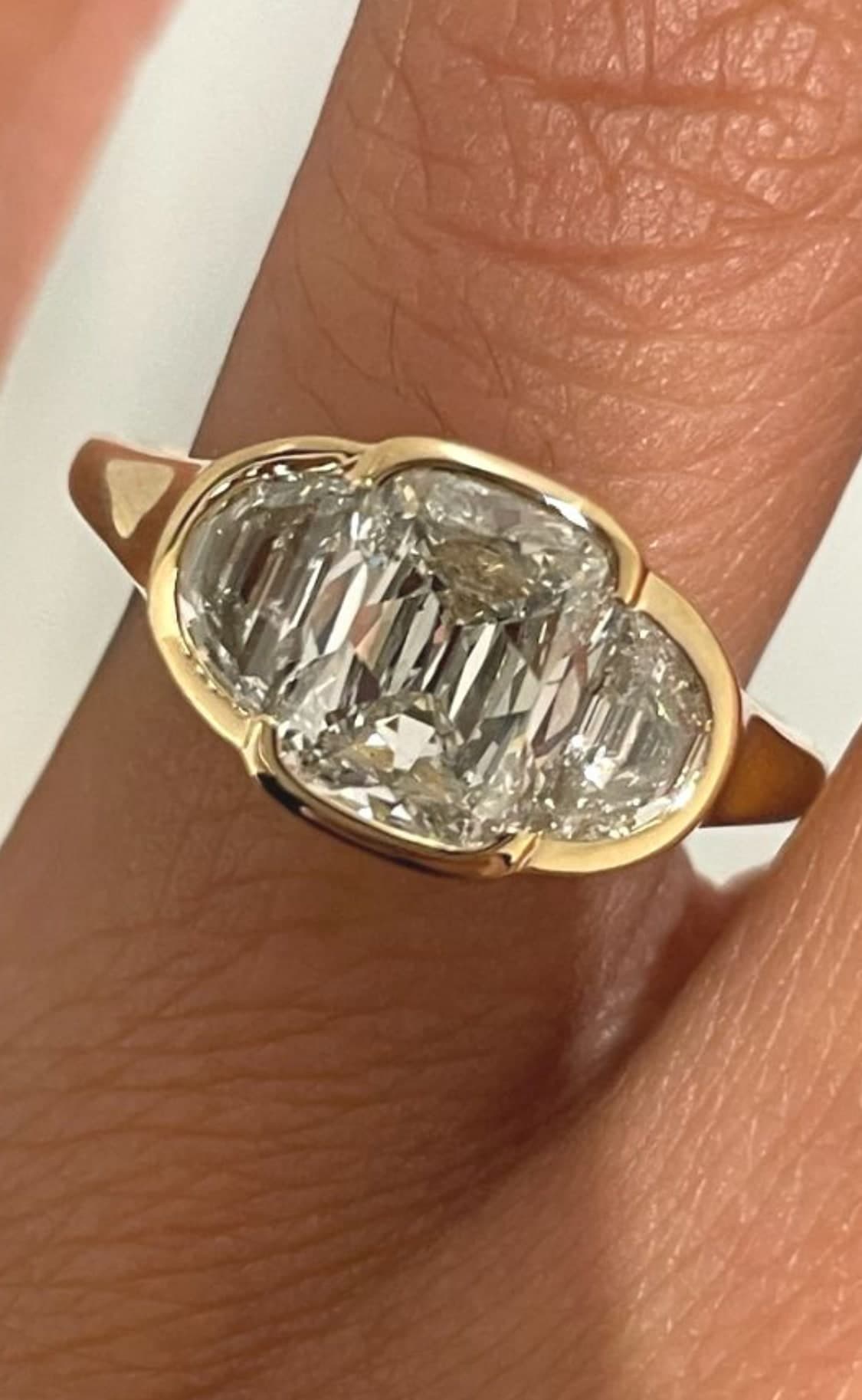 Three-stone bezel-set diamond ring in yellow gold worn on a finger