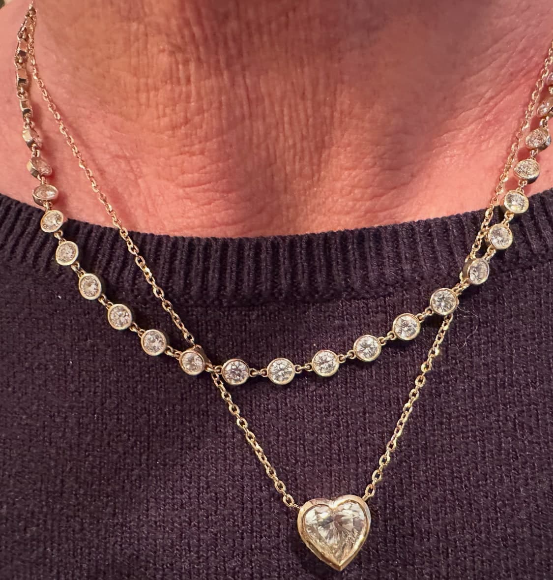 Layered diamond necklaces — bezel-set station chain with a heart-shaped diamond pendant