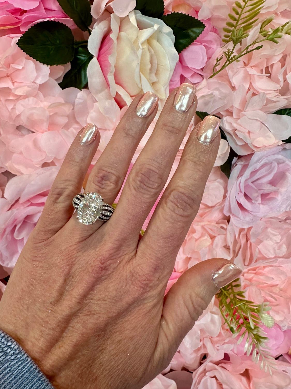 Oval brilliant diamond ring with sculpted split-shank pavé band, worn against a floral wall